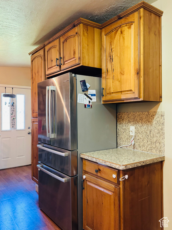 Kitchen featuring freestanding refrigerator, brown cabinetry, light countertops, and a textured ceiling