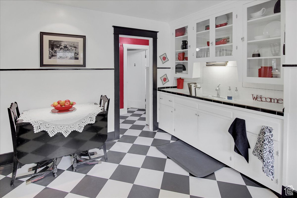 Kitchen with dark flooring, tile countertops, white cabinetry, backsplash, and glass insert cabinets