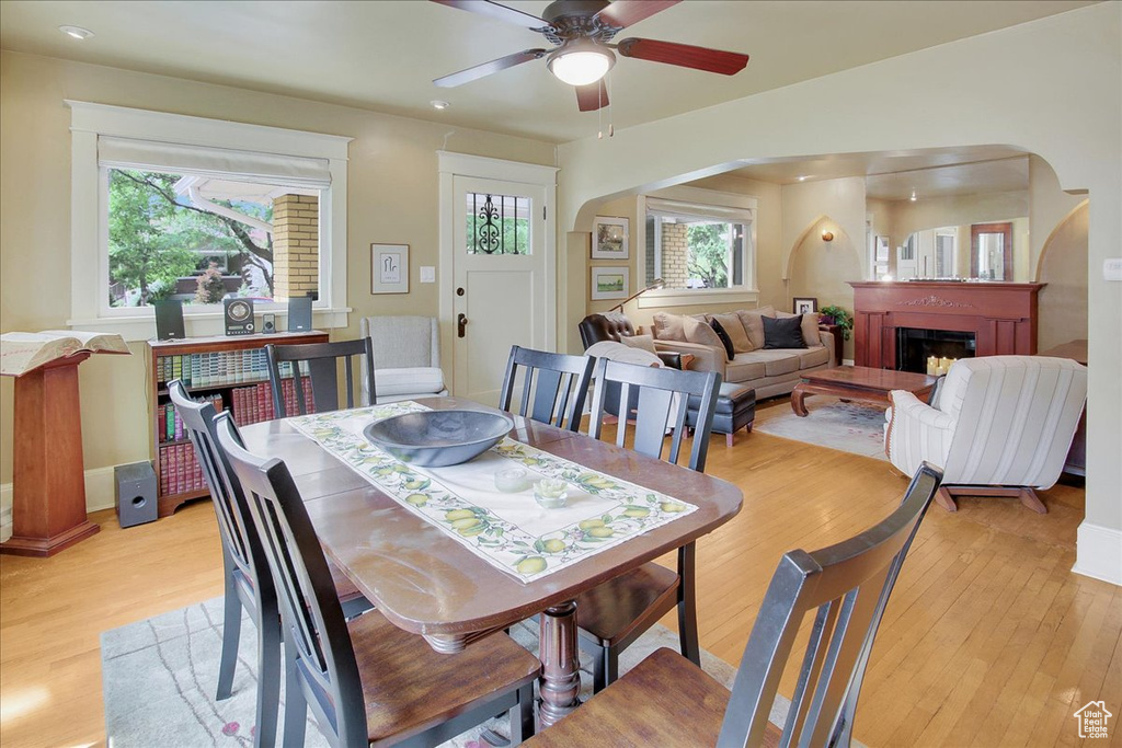 Dining room with arched walkways, light wood-style floors, ceiling fan, and a fireplace