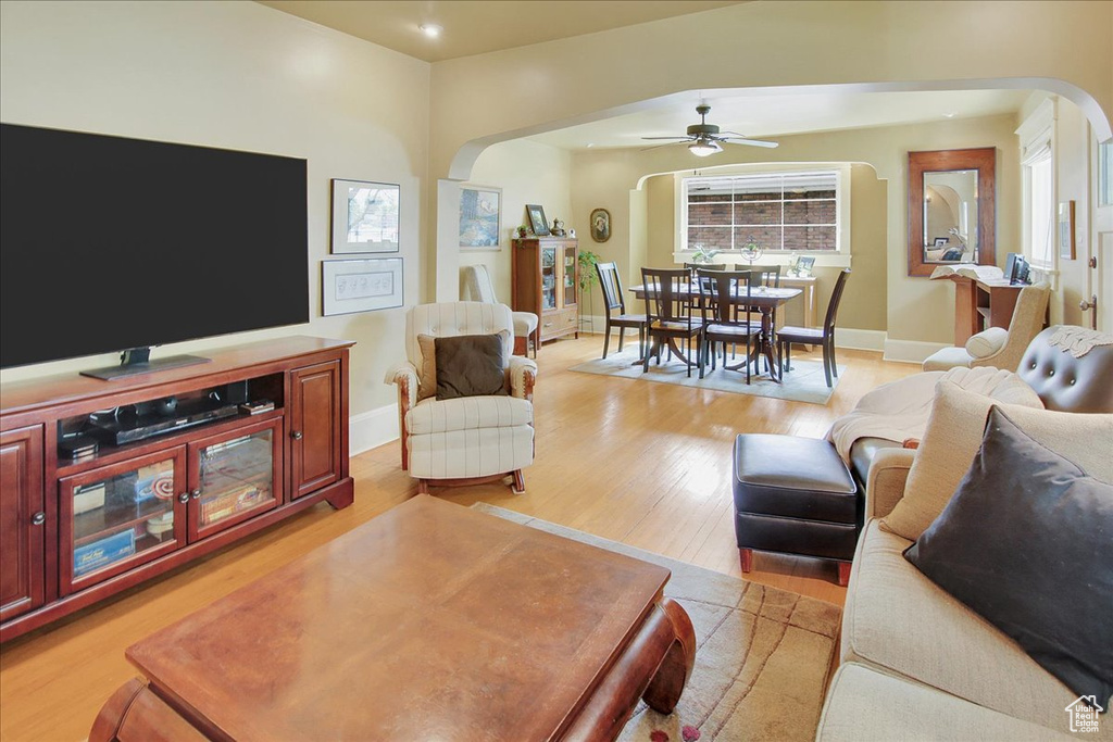 Living area with arched walkways, ceiling fan, light wood-type flooring, and baseboards