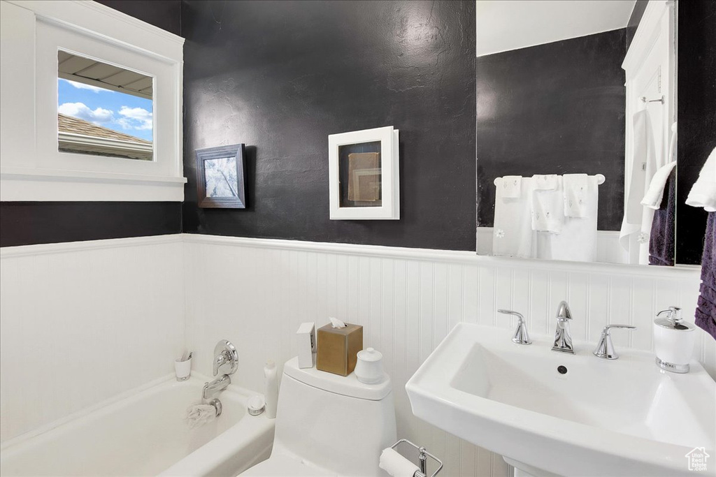 Full bath featuring a sink, a wainscoted wall, a bath, and toilet