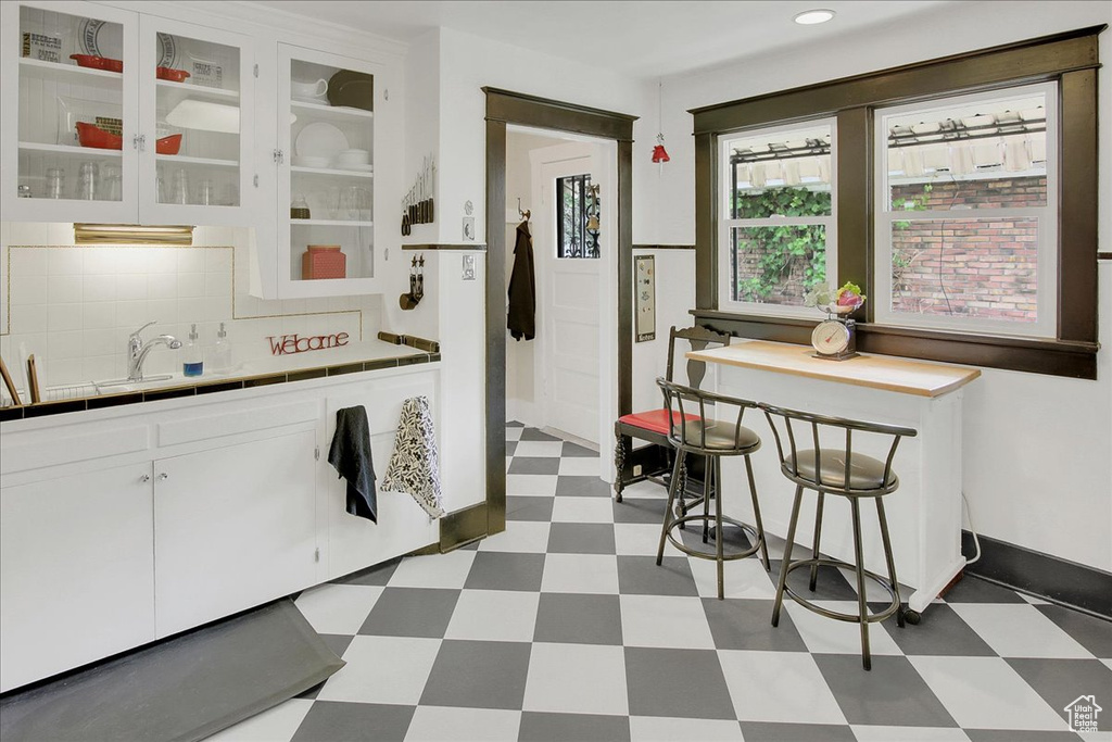 Kitchen featuring tile patterned floors, tile counters, white cabinetry, backsplash, and glass insert cabinets