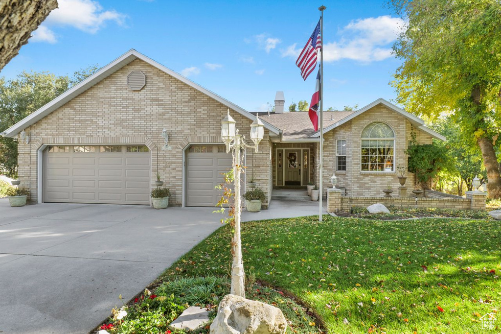 Ranch-style house with brick siding, a garage, driveway, a front yard, and a chimney