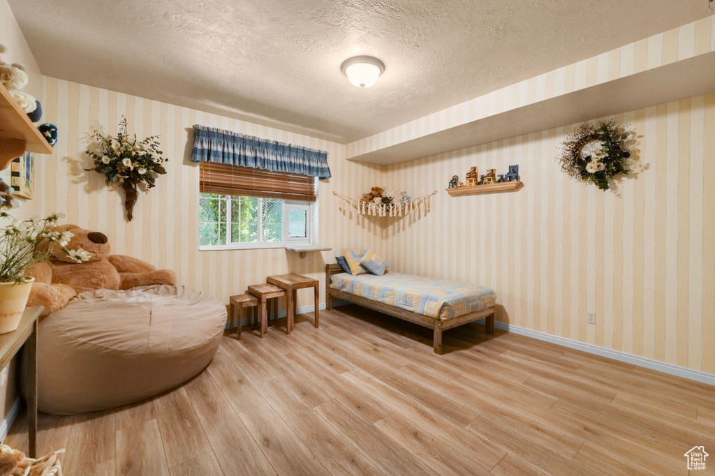 Bedroom featuring wallpapered walls, light wood-style flooring, a textured ceiling, and baseboards