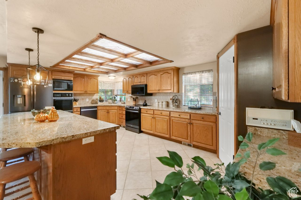 Kitchen featuring black appliances, light tile patterned floors, decorative backsplash, a kitchen breakfast bar, and light stone countertops