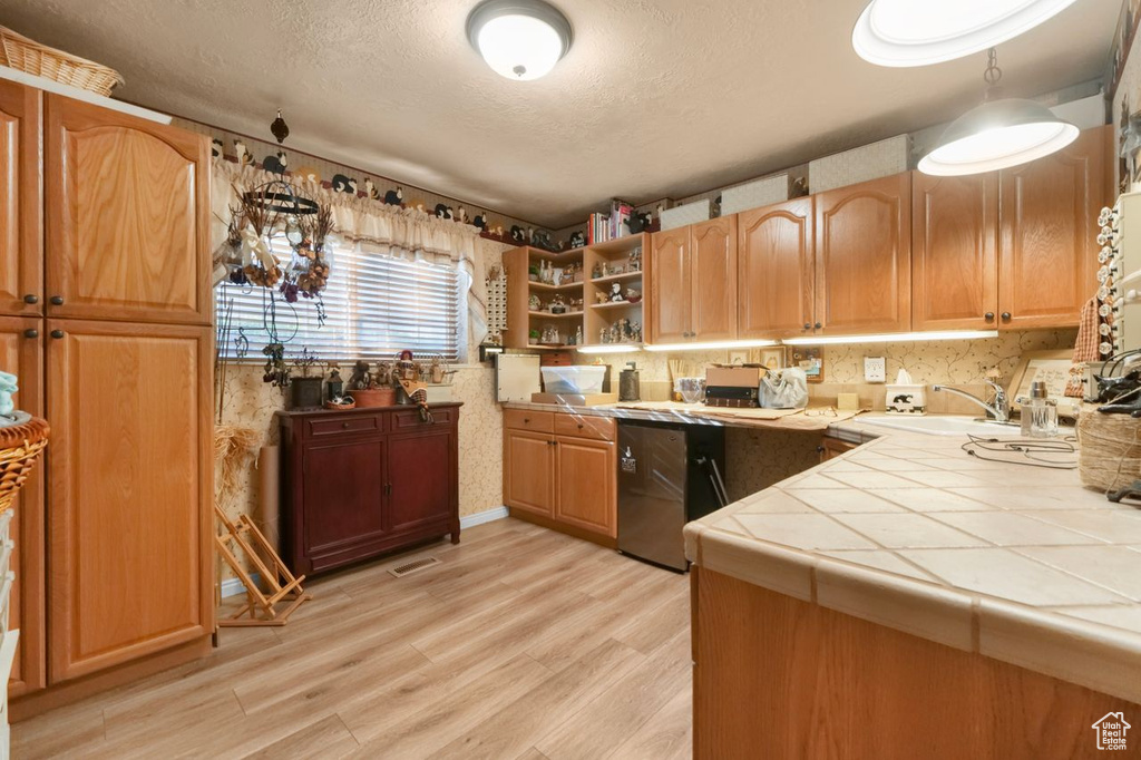 Kitchen featuring tile counters, a sink, a textured ceiling, light wood-style flooring, and open shelves