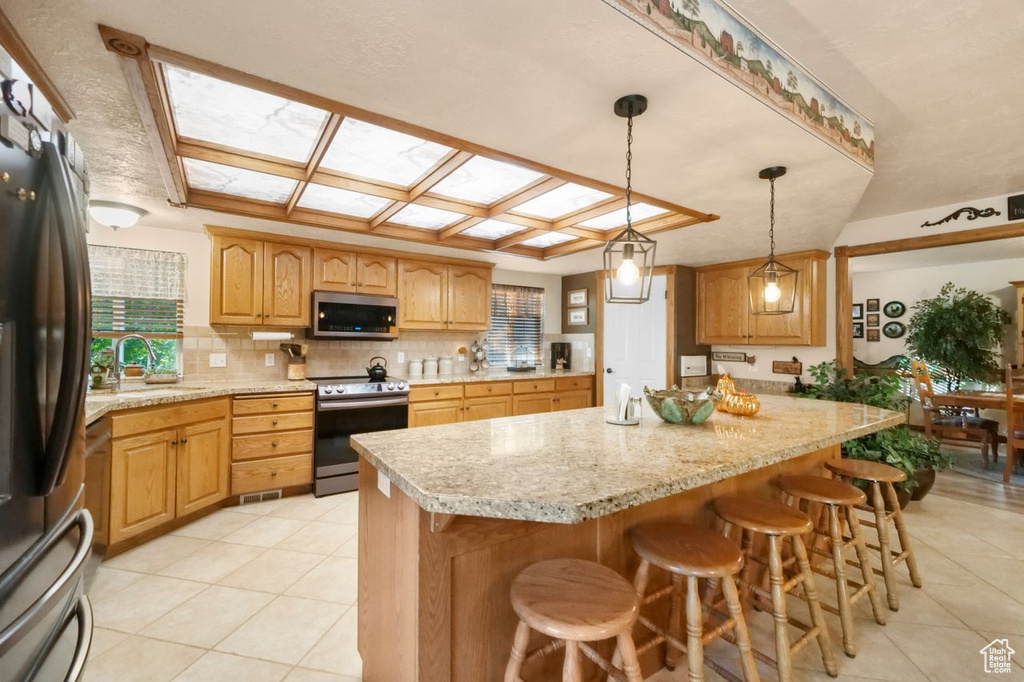 Kitchen with appliances with stainless steel finishes, a sink, light tile patterned flooring, a kitchen breakfast bar, and decorative backsplash
