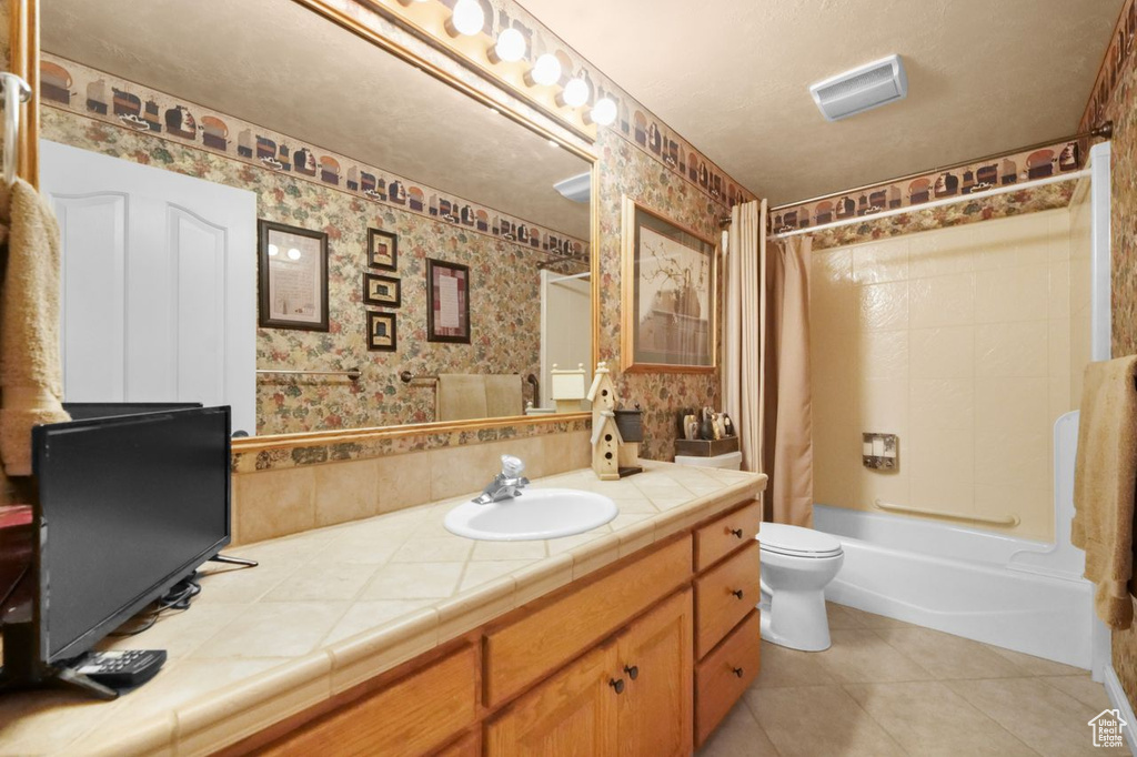 Bathroom with vanity, shower / bathtub combination with curtain, toilet, tile patterned floors, and wallpapered walls