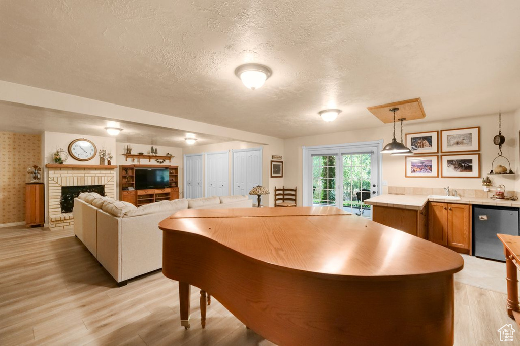 Dining area with a textured ceiling, wet bar, light wood-type flooring, a brick fireplace, and baseboards