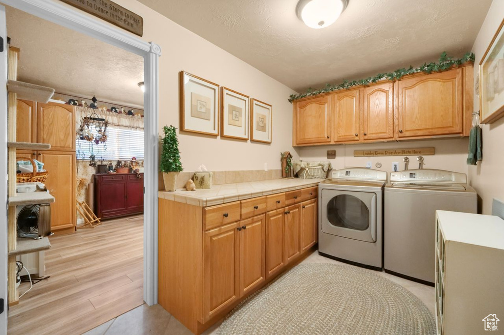 Washroom featuring washer and clothes dryer, cabinet space, light wood finished floors, and a textured ceiling