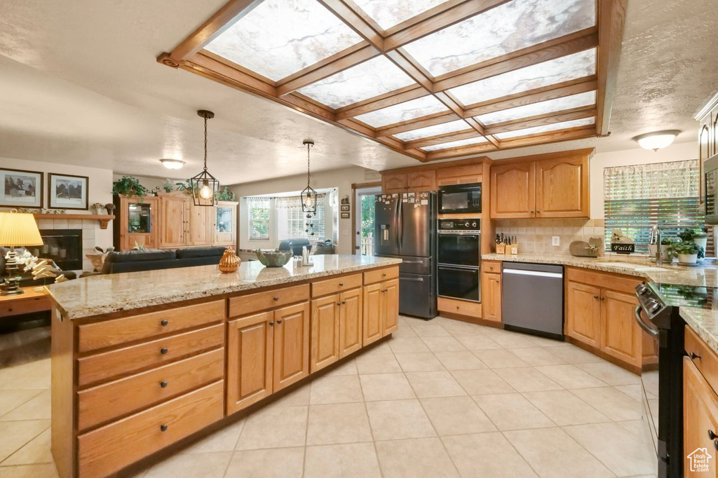 Kitchen featuring black appliances, a kitchen island, tasteful backsplash, light tile patterned flooring, and a tiled fireplace