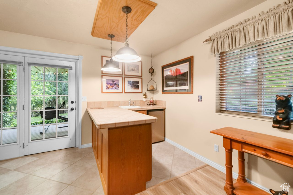 Kitchen featuring a peninsula, tile counters, fridge, light tile patterned flooring, and hanging light fixtures