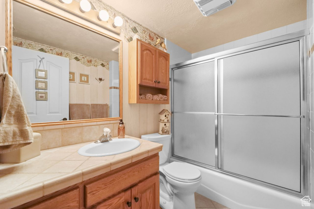 Bathroom featuring toilet, vanity, bath / shower combo with glass door, and a textured ceiling
