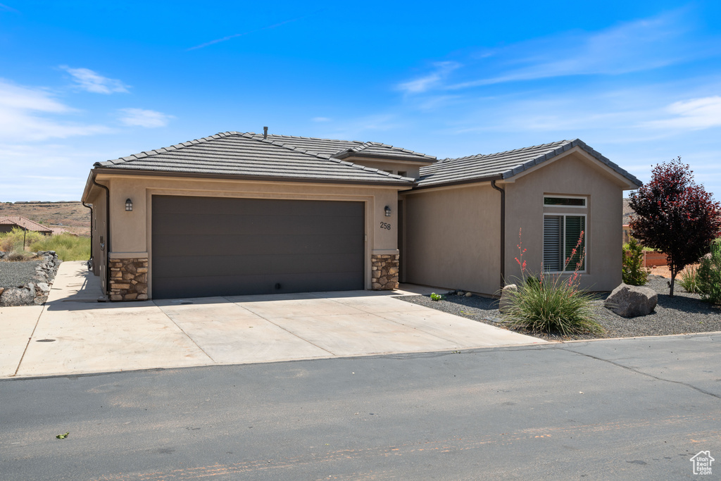 View of front of home featuring a garage, stone siding, driveway, and a tiled roof