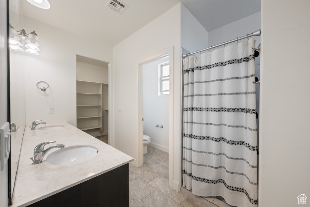 Bathroom with toilet, double vanity, and curtained shower