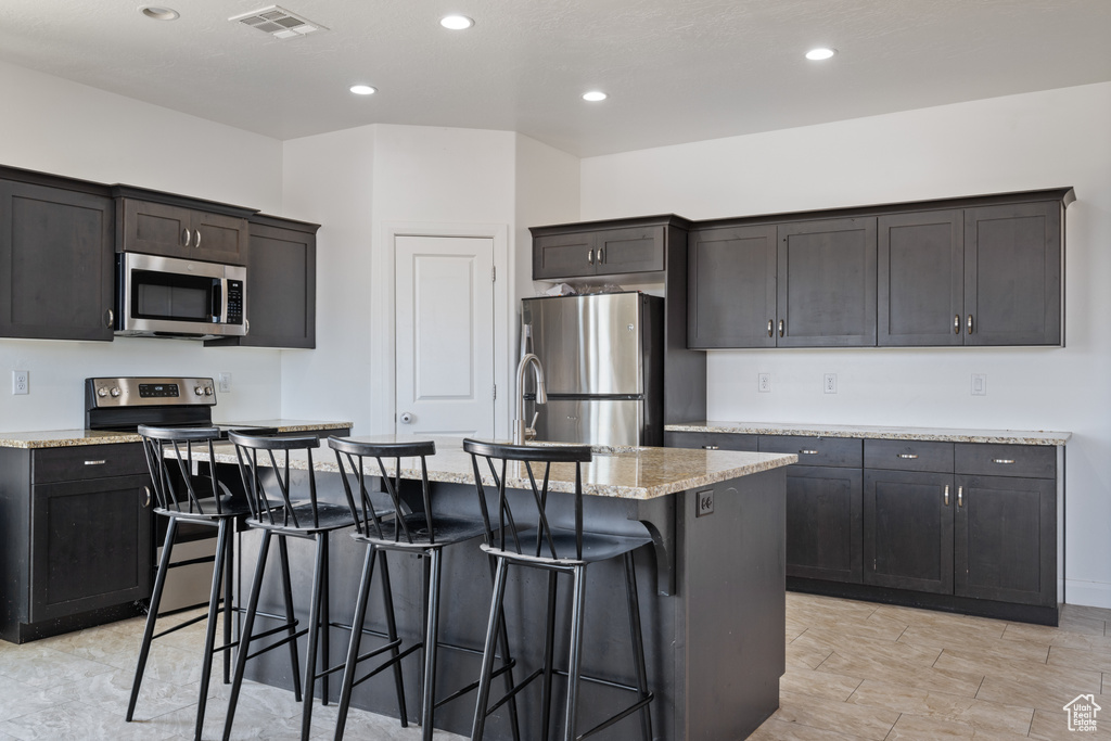 Kitchen featuring appliances with stainless steel finishes, a breakfast bar, a kitchen island with sink, recessed lighting, and light stone countertops