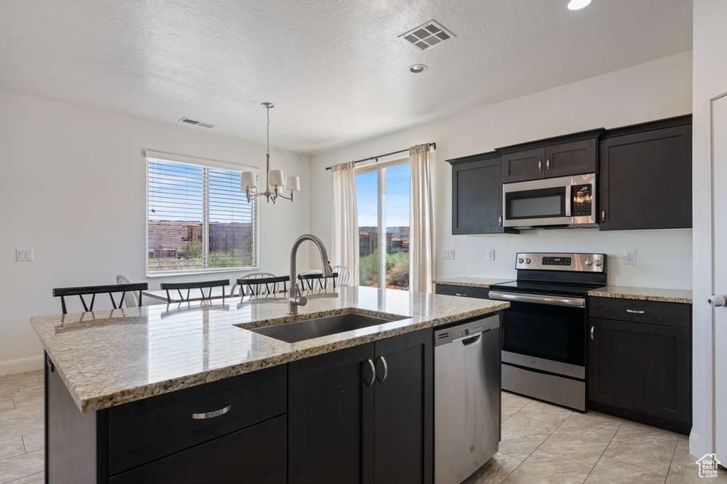 Kitchen with stainless steel appliances, a sink, a chandelier, a center island with sink, and hanging light fixtures