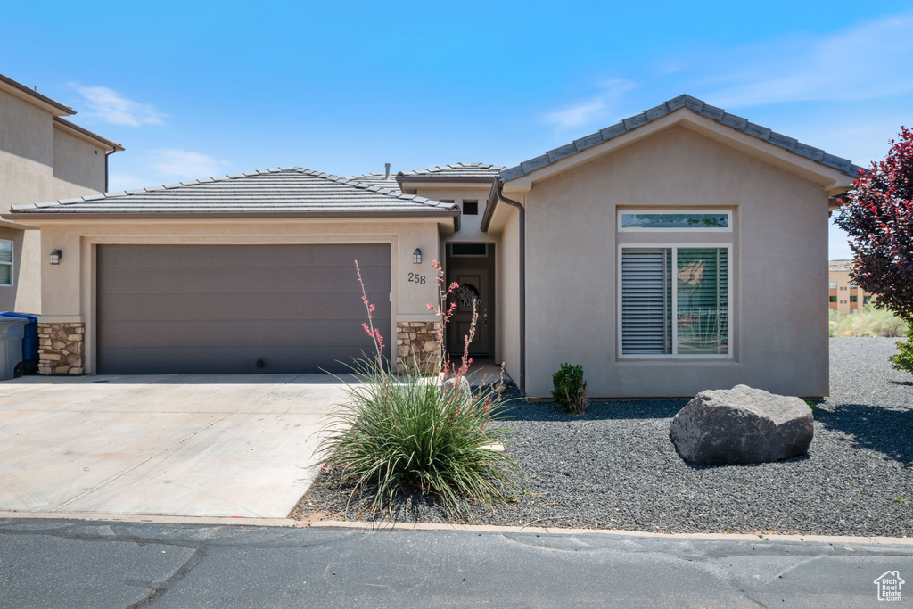 View of front of house featuring an attached garage, driveway, stucco siding, and a tile roof