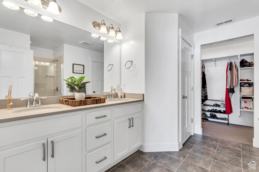 Full bathroom featuring double vanity, a stall shower, a walk in closet, tile patterned floors, and baseboards