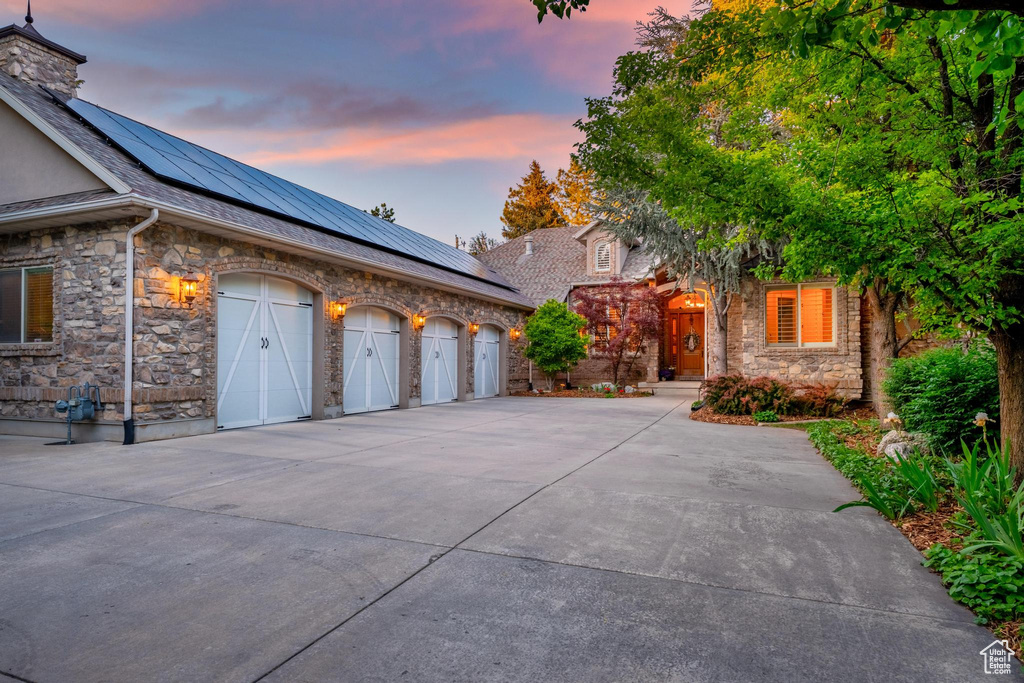 View of front of property featuring stone siding, driveway, solar panels, and a garage