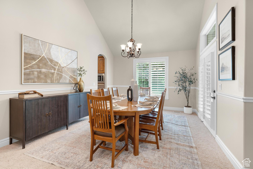 Dining space featuring a chandelier, light carpet, arched walkways, and high vaulted ceiling