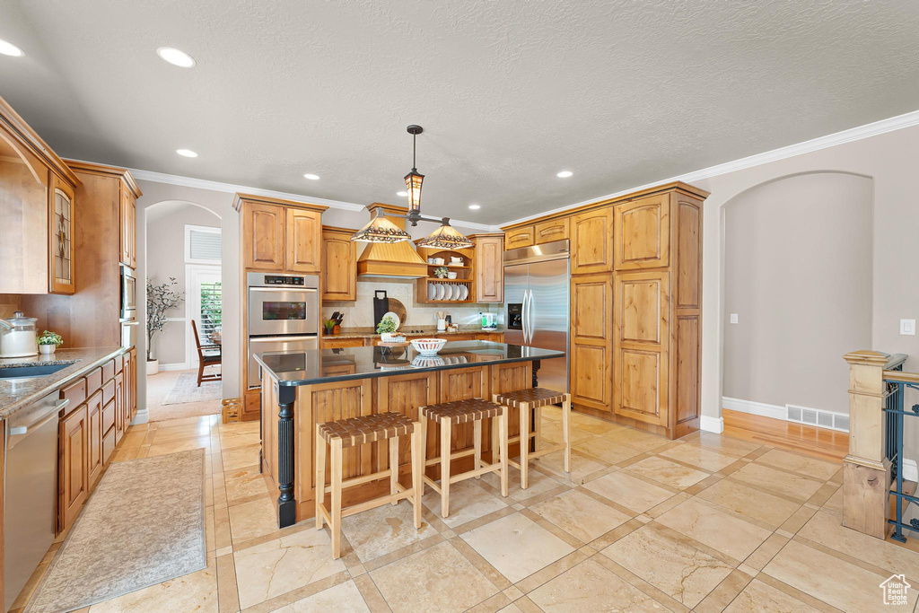 Kitchen with arched walkways, stainless steel appliances, ornamental molding, a kitchen bar, and recessed lighting