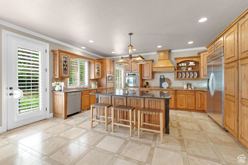Kitchen with built in appliances, open shelves, custom range hood, ornamental molding, and a kitchen island
