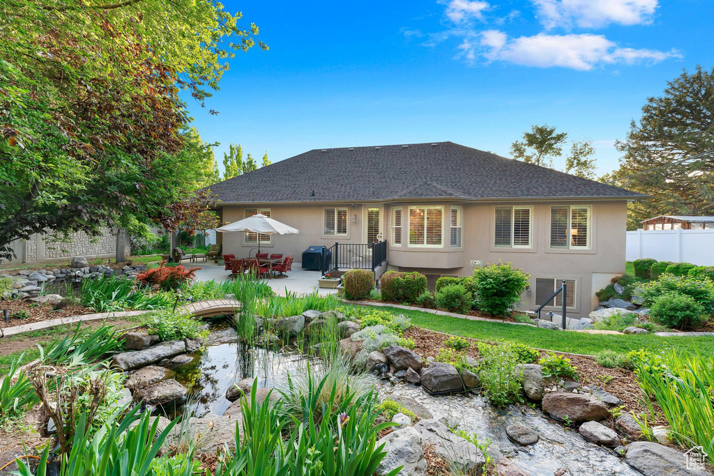 Rear view of house with stucco siding, a small pond, a patio, and a shingled roof