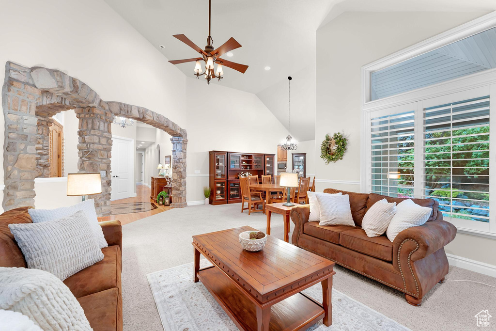 Living room featuring decorative columns, light colored carpet, high vaulted ceiling, arched walkways, and a ceiling fan