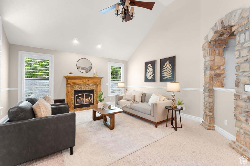 Living room with a glass covered fireplace, a ceiling fan, plenty of natural light, carpet flooring, and high vaulted ceiling