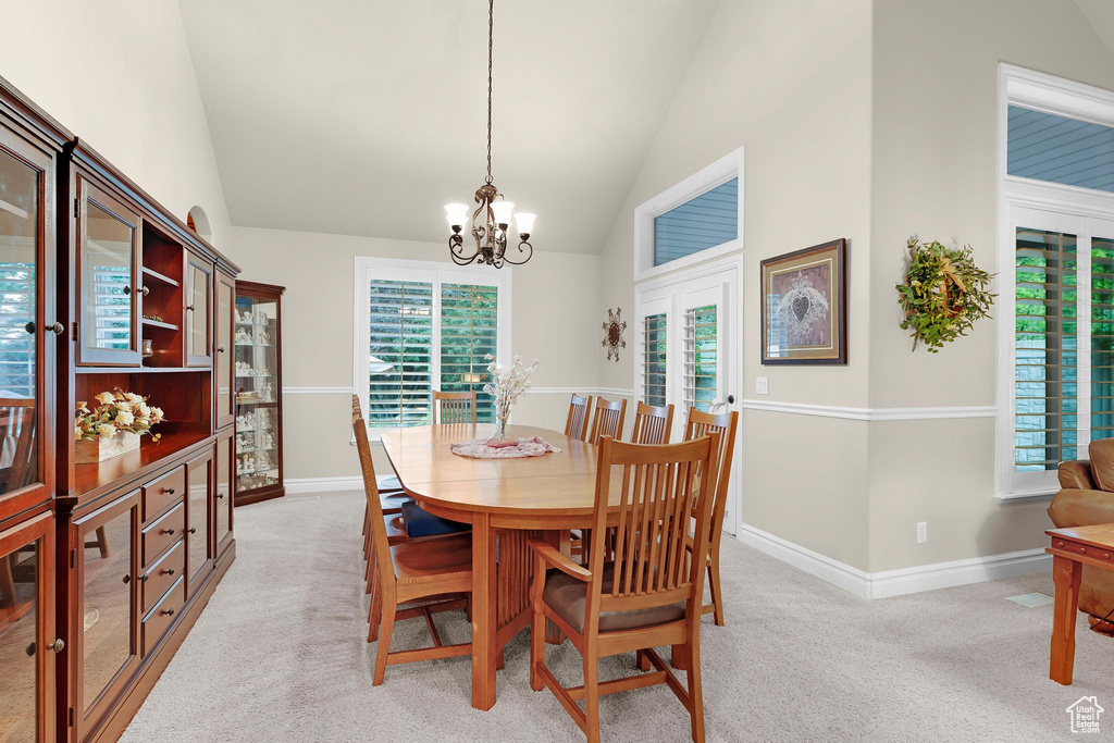 Dining area with light carpet, a chandelier, plenty of natural light, baseboards, and high vaulted ceiling