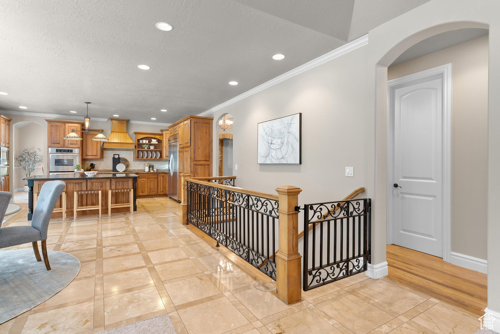 Hallway featuring arched walkways, recessed lighting, ornamental molding, an upstairs landing, and a textured ceiling