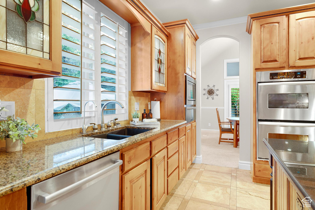 Kitchen with appliances with stainless steel finishes, a sink, arched walkways, light stone counters, and glass insert cabinets