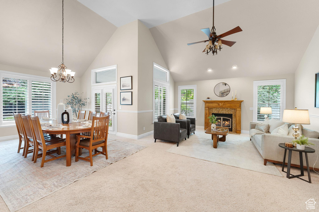 Dining room with a warm lit fireplace, a chandelier, light colored carpet, a ceiling fan, and high vaulted ceiling