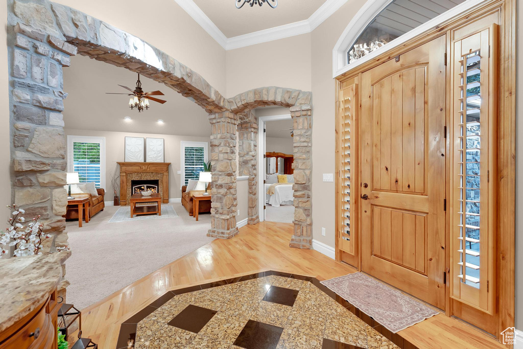 Foyer entrance featuring decorative columns, ornamental molding, ceiling fan, wood finished floors, and arched walkways