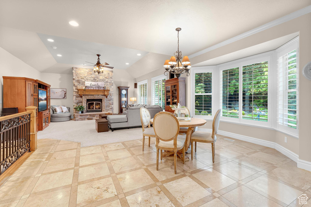 Dining area featuring a stone fireplace, ceiling fan, inlaid floor details, a chandelier, and lofted ceiling