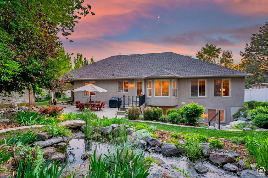 Back of house at dusk with stucco siding, a small pond, a patio area, and outdoor dining area
