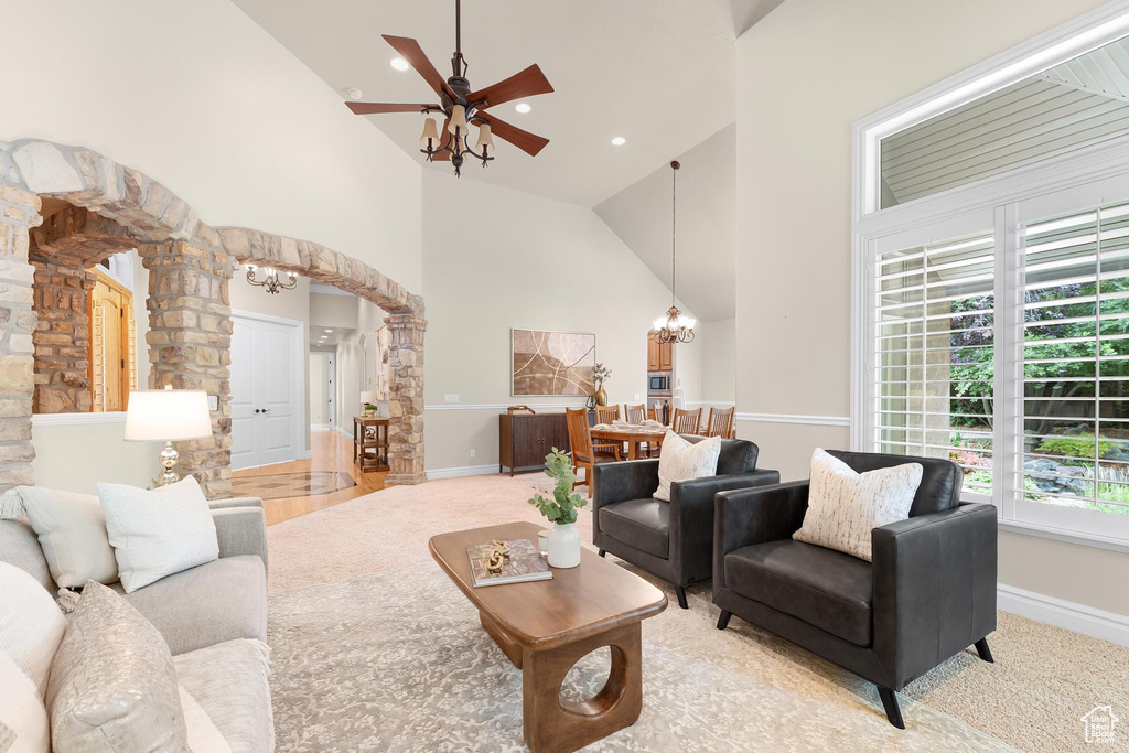 Carpeted living area featuring decorative columns, arched walkways, high vaulted ceiling, a chandelier, and a ceiling fan