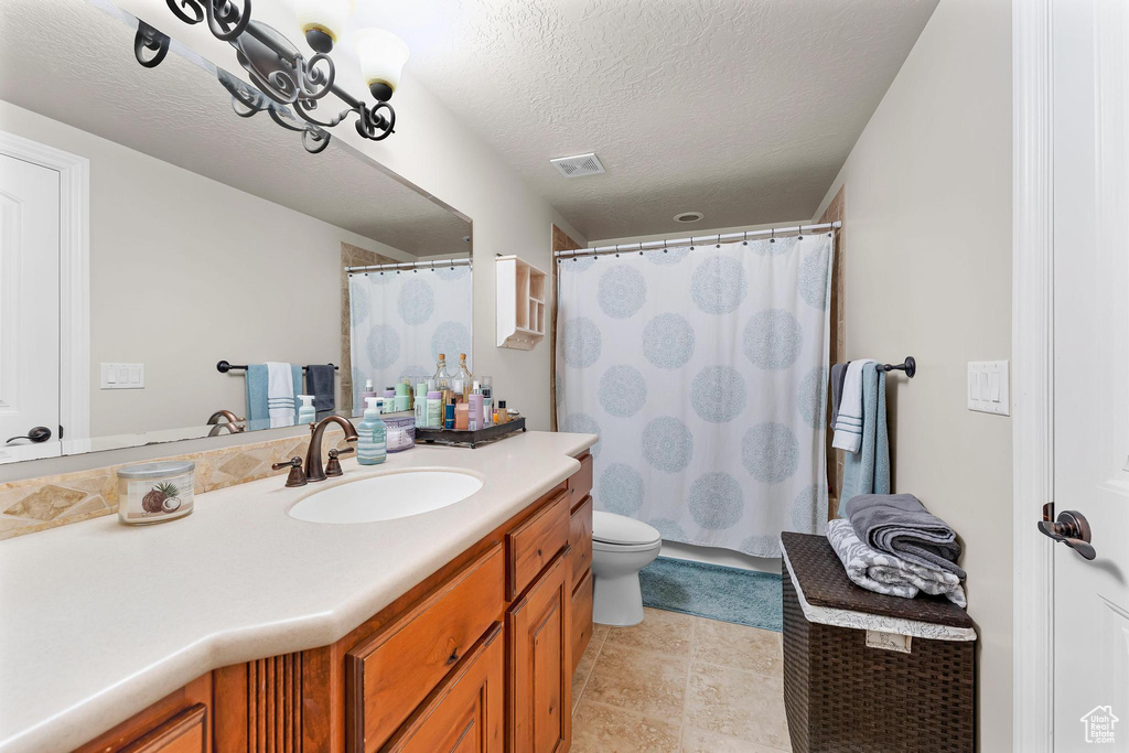 Full bathroom with vanity, toilet, curtained shower, and a textured ceiling