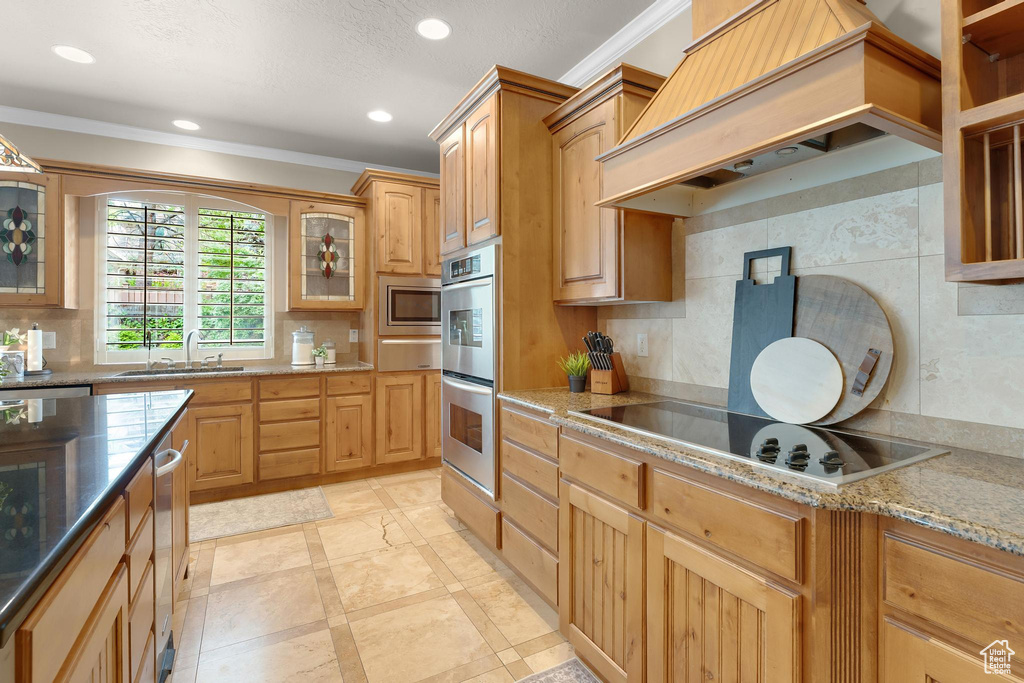Kitchen with premium range hood, appliances with stainless steel finishes, tasteful backsplash, ornamental molding, and light stone countertops
