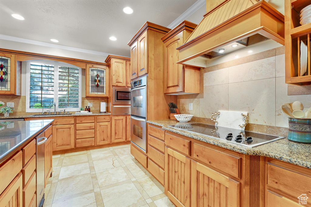 Kitchen with appliances with stainless steel finishes, ornamental molding, a sink, custom exhaust hood, and light stone countertops