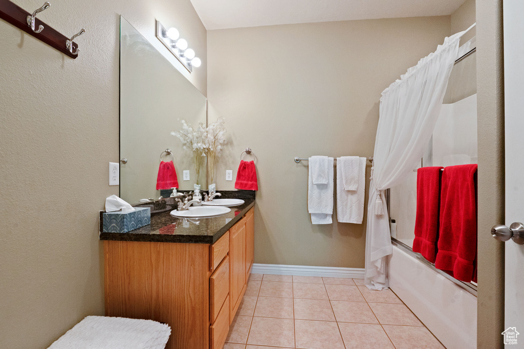 Full bath with shower / tub combo, double vanity, tile patterned flooring, and baseboards