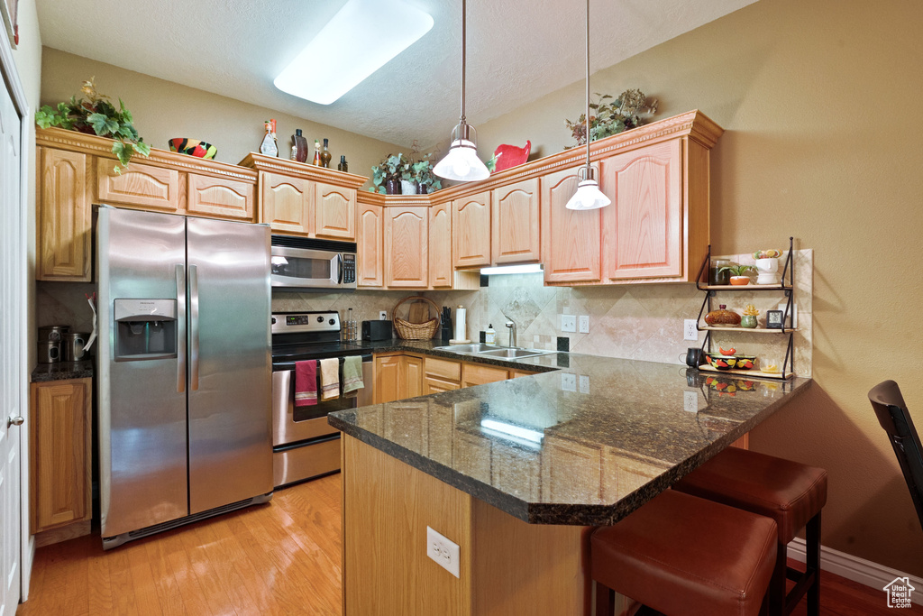 Kitchen featuring stainless steel appliances, a sink, a peninsula, and light wood-type flooring