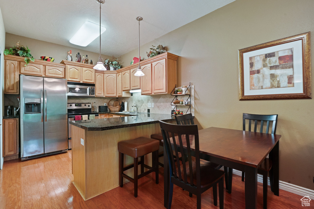 Kitchen with appliances with stainless steel finishes, decorative backsplash, a peninsula, a sink, and light brown cabinetry