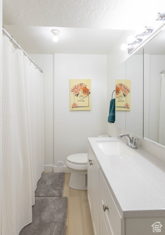 Bathroom featuring toilet, vanity, a shower with curtain, a textured ceiling, and wood finished floors