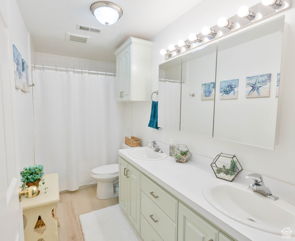 Full bath with double vanity, toilet, a shower with shower curtain, and wood finished floors