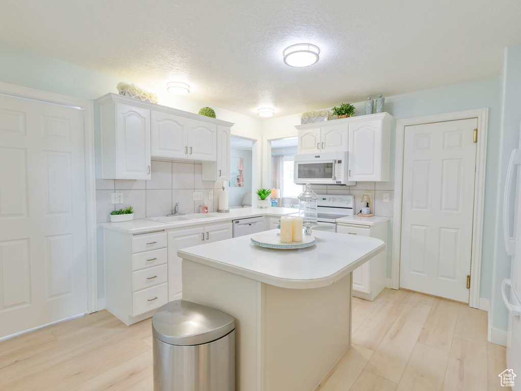 Kitchen featuring white appliances, a sink, light countertops, decorative backsplash, and a textured ceiling