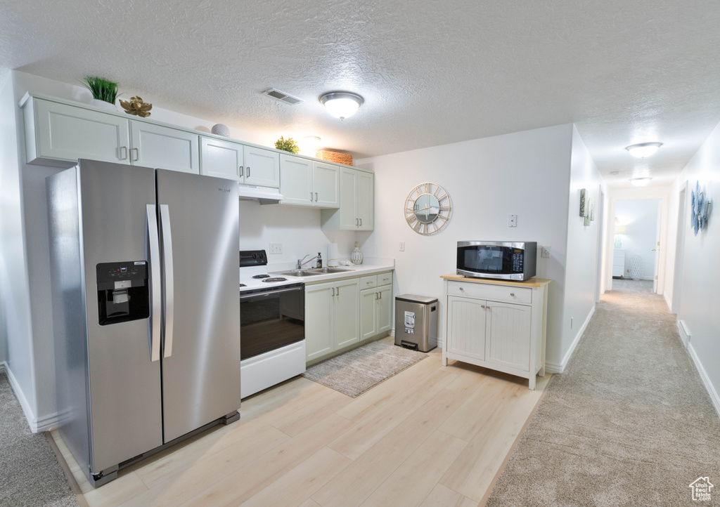 Kitchen with appliances with stainless steel finishes, a sink, under cabinet range hood, a textured ceiling, and light countertops