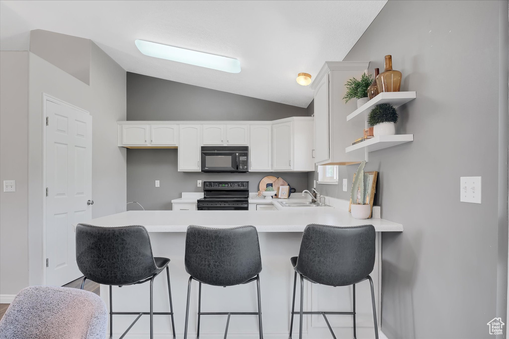 Kitchen with black appliances, a sink, a peninsula, lofted ceiling, and white cabinets