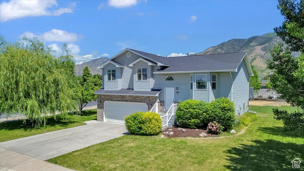 View of front of property with a mountain view, brick siding, driveway, and a front lawn